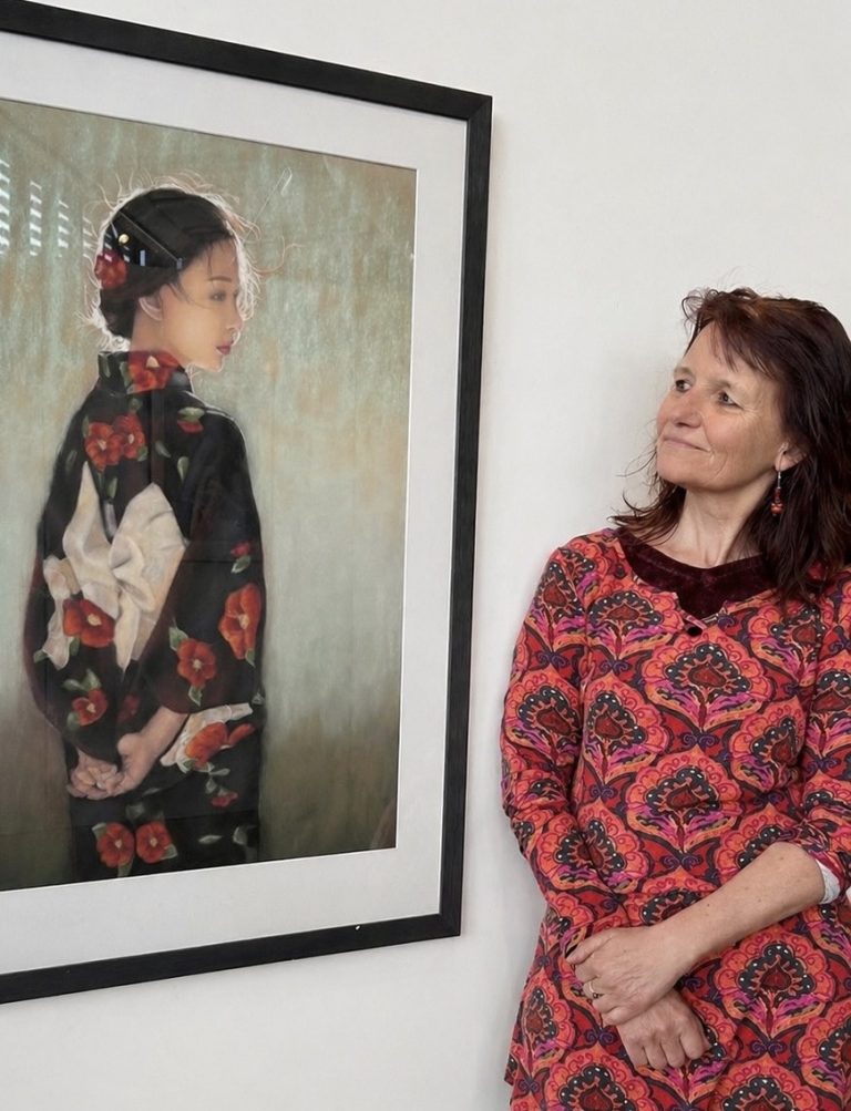 Photographie de Sylvie Sanséau, artiste peintre pastelliste, installée dans le Grand Genève, exposant aux Nations Unies, à Genève. Elle regarde son tableau pastel d'une femme en kimono, comme si elle dialoguait avec le portrait pastel.